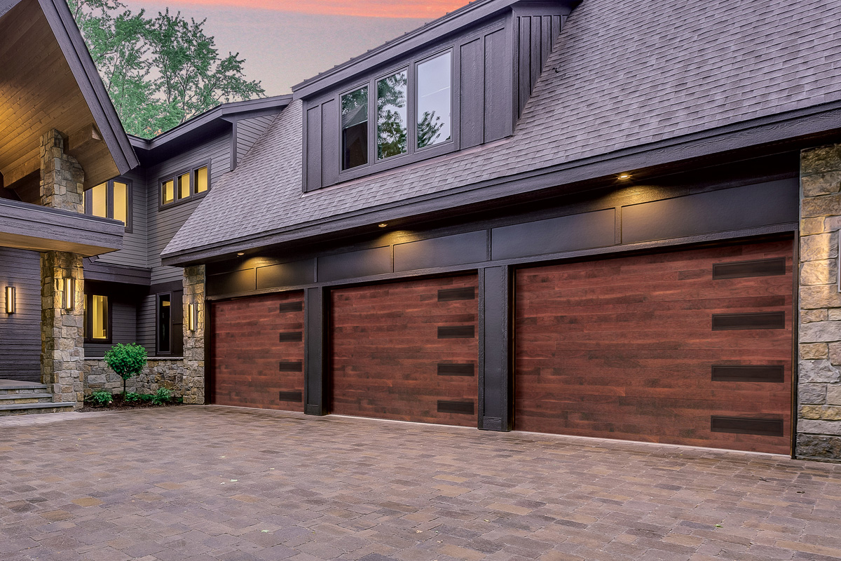 Modern luxury home featuring three dark wood-grain garage doors with horizontal window inserts in a paved driveway.